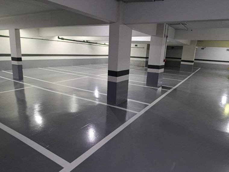 Garagem de condomínio com piso epóxi cinza e vagas demarcadas em branco
